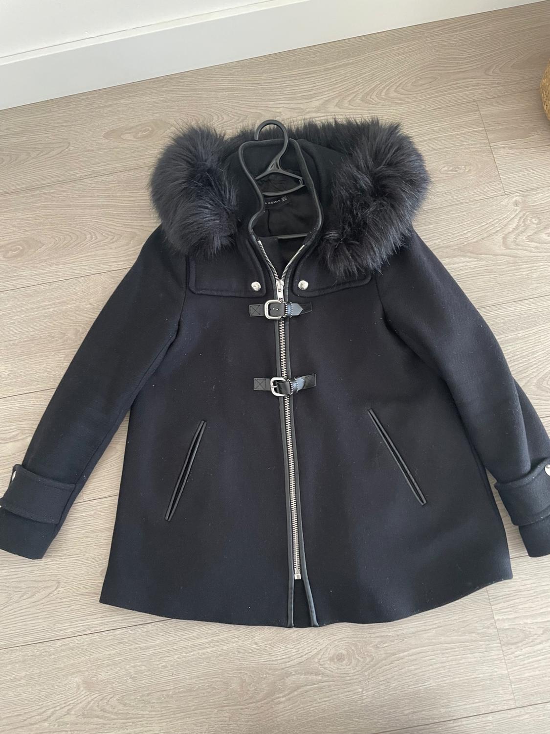 Black coat with a faux fur hood, zip and buckle fastening, on a light wooden floor.