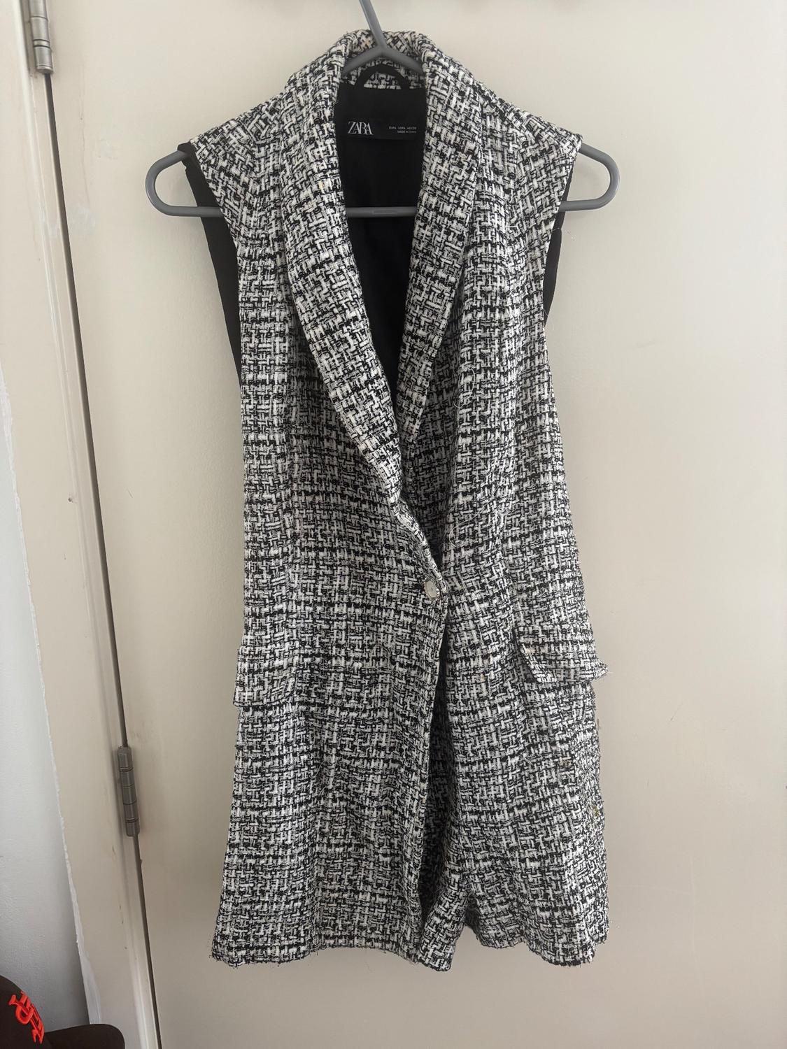 Black and white sleeveless waistcoat with a woven design, hanging on a hanger. Visible label with the ZARA brand.