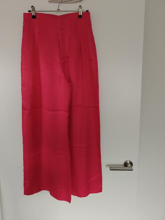 Bright red trousers hanging on a hanger over a white door with a silver handle.