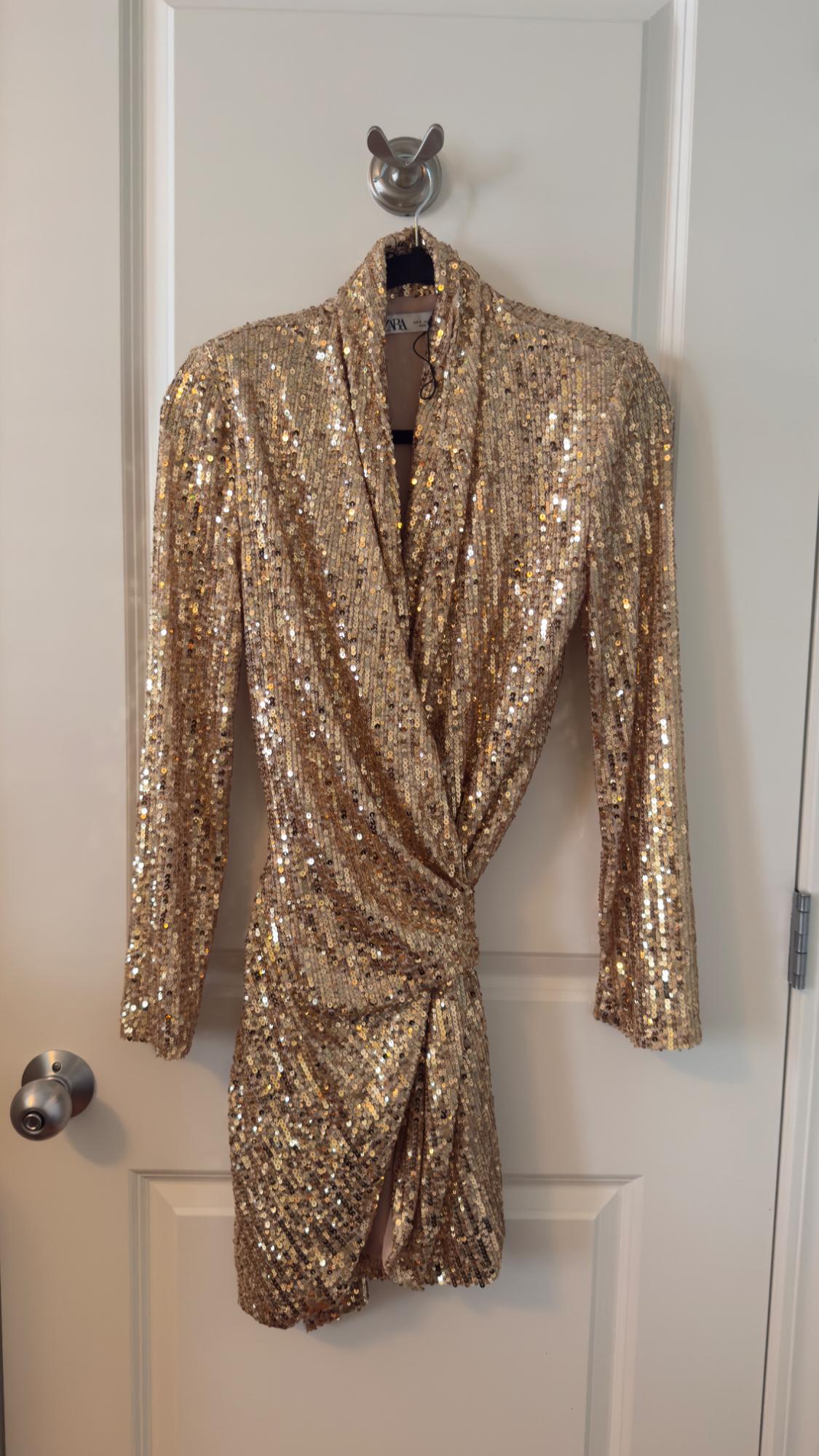 Gold sequin dress hanging on a white door. Wrap design with long sleeves and draped waist detail.