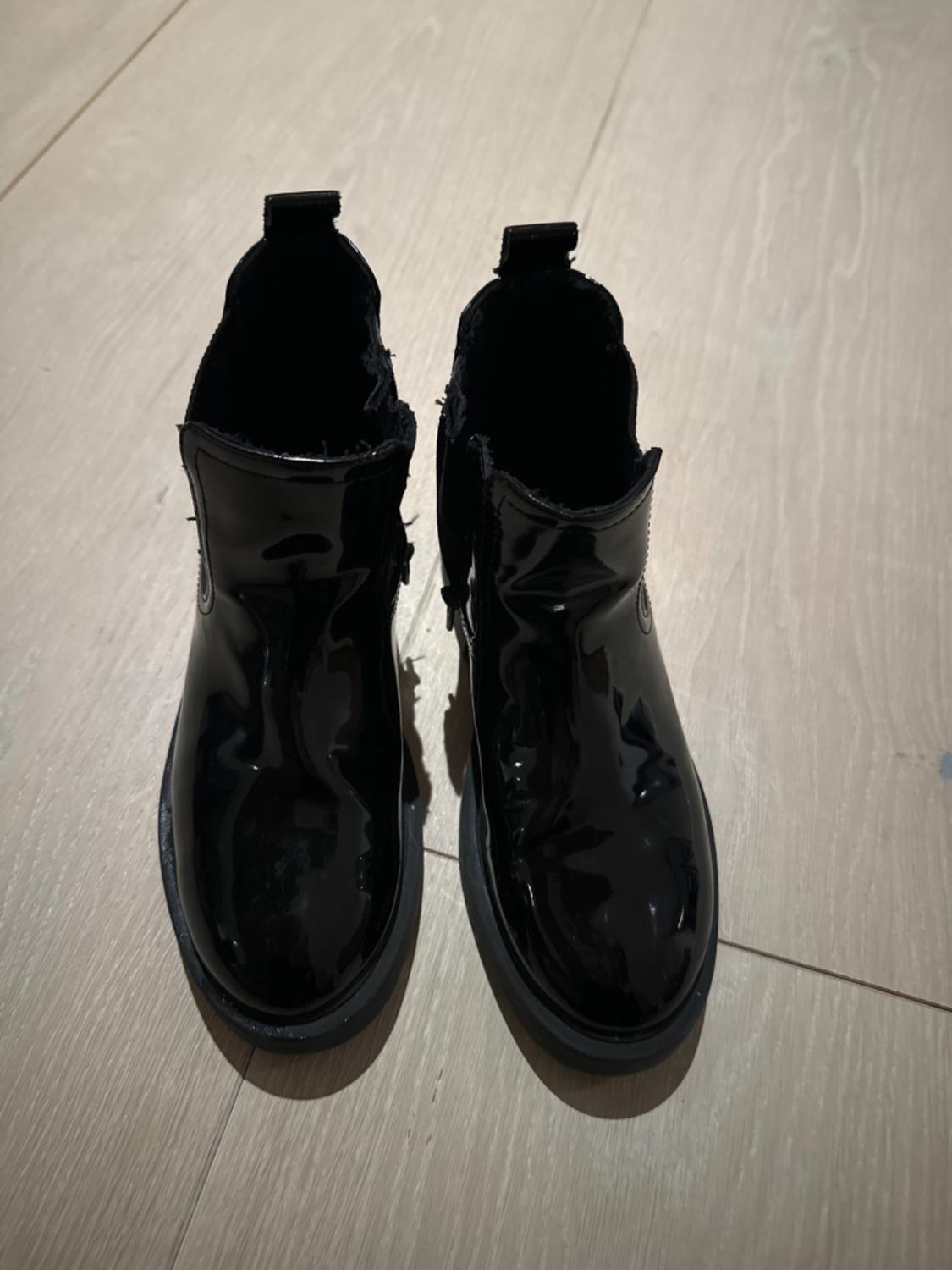 Black patent leather boots viewed from above on a light wooden floor.