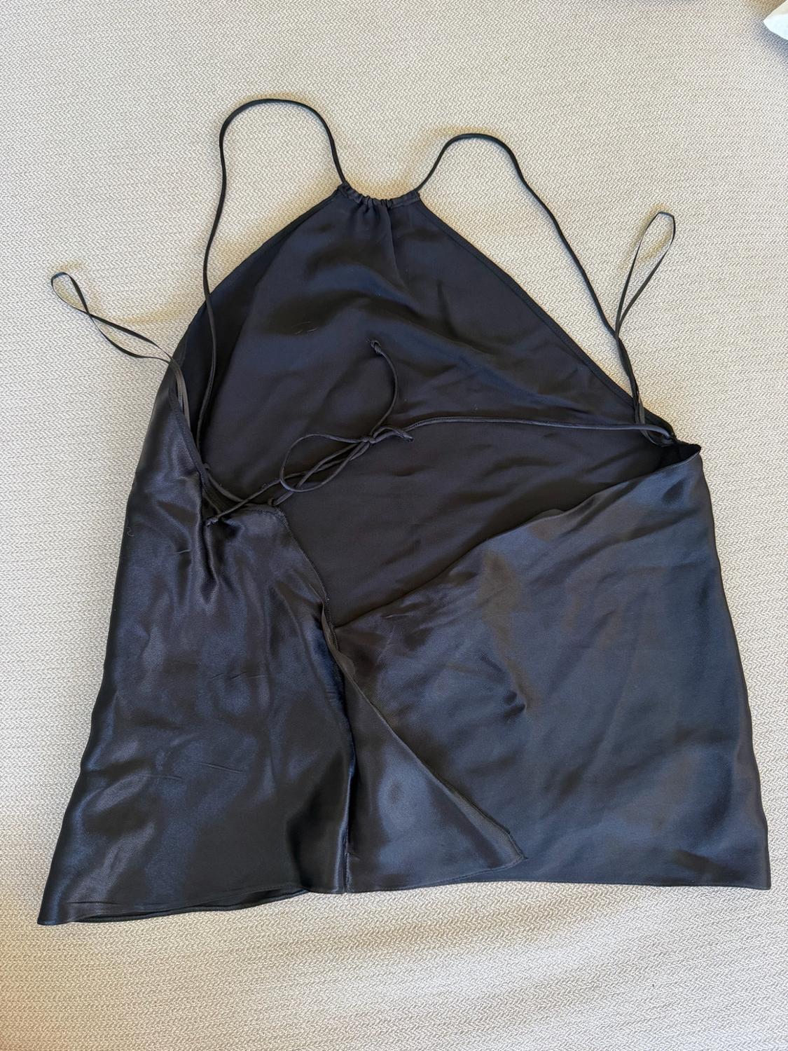 Black satin top viewed from the back, with thin straps tied at the back, laid out on a light-coloured surface.