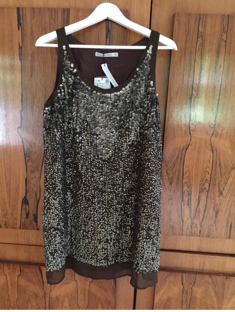Front view of a sleeveless blouse with silver sequins and a brown background.
