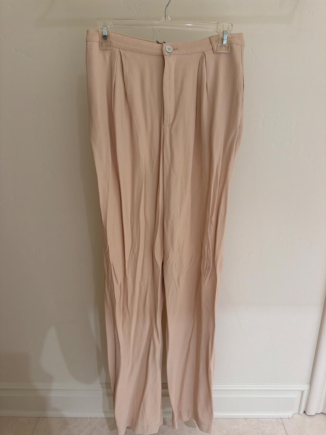 Beige lightweight fabric trousers hanging on a clear hanger against a white wall.