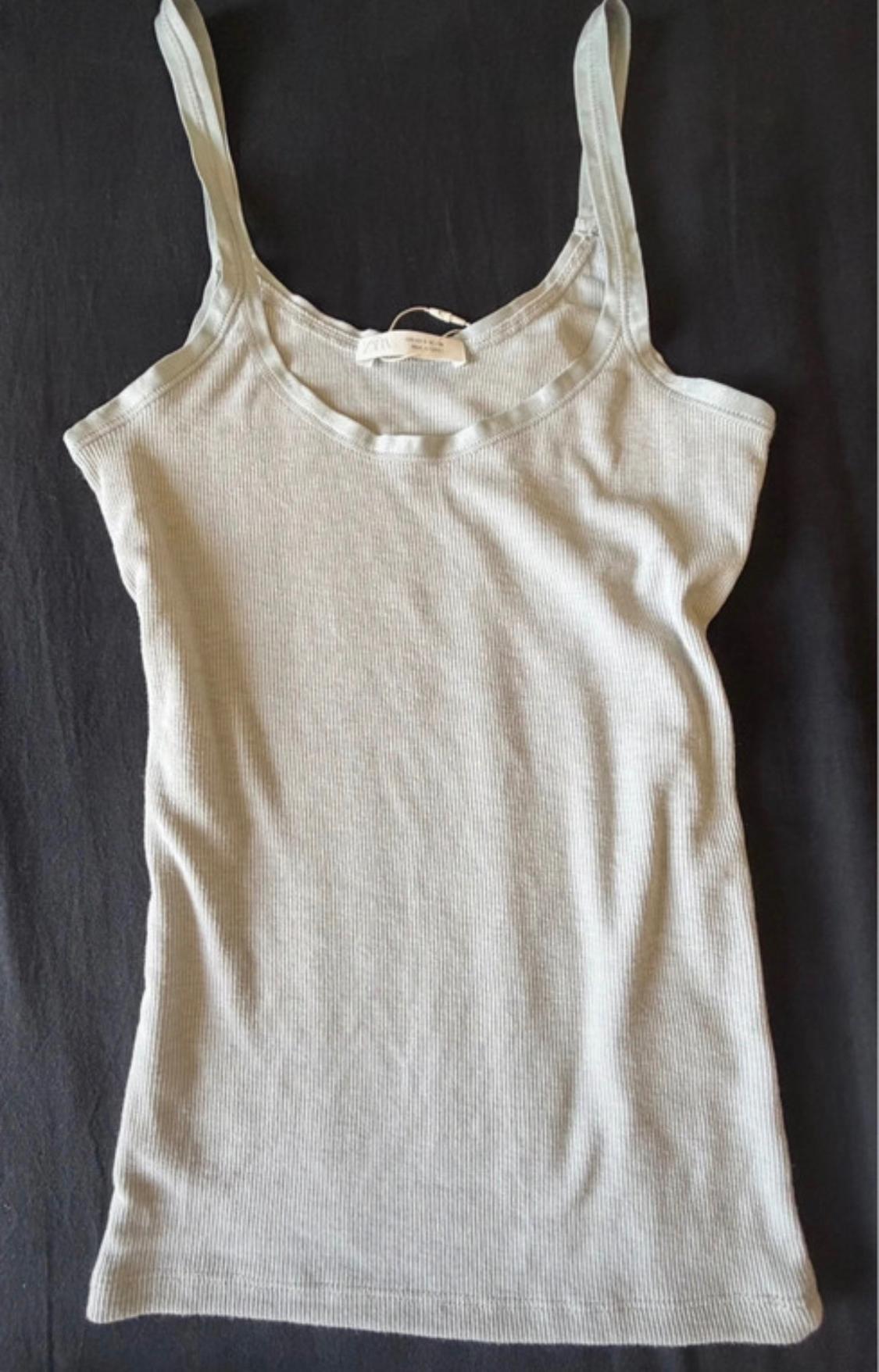 Light grey ribbed basic vest top with a round neck, laid against a dark fabric background.