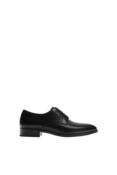 Side view of a black derby shoe, plain upper, round toe last, sole with a slight heel.