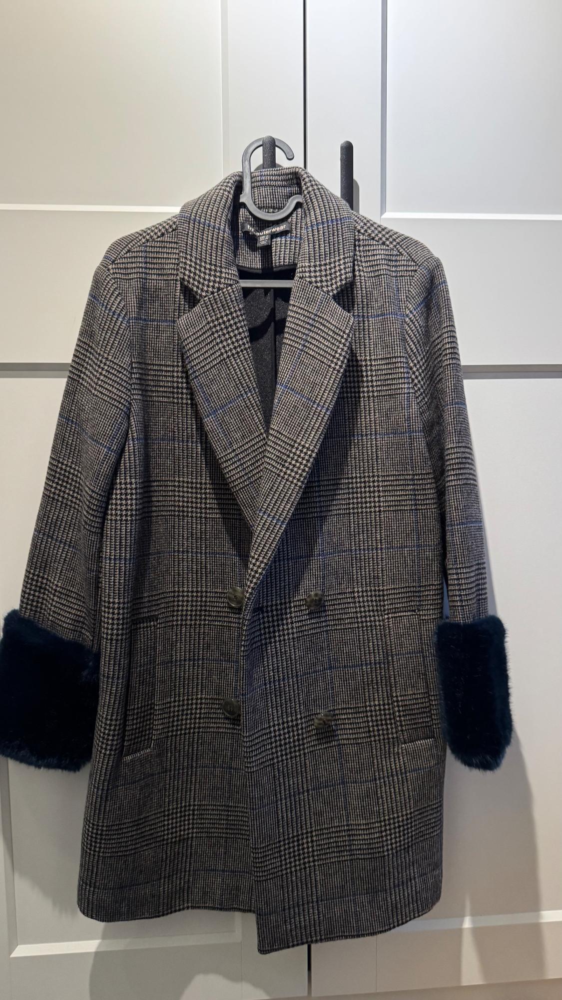 Grey checked coat with black faux fur cuffs, hanging on a hanger against a white background.