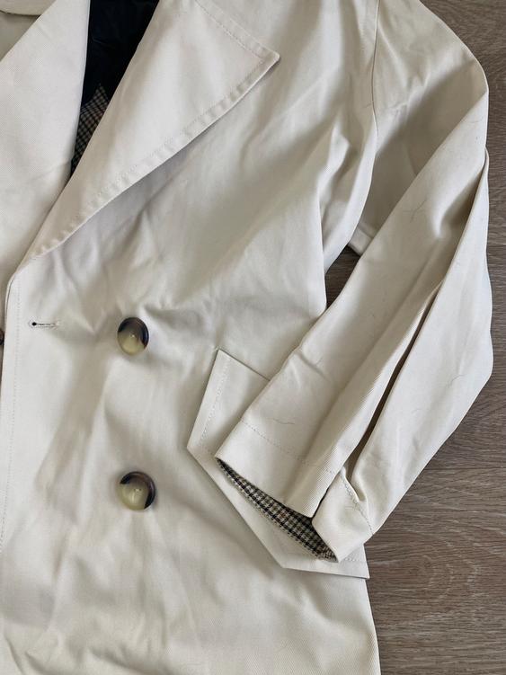 Beige coat with large buttons and plaid lining, on a light wooden surface.