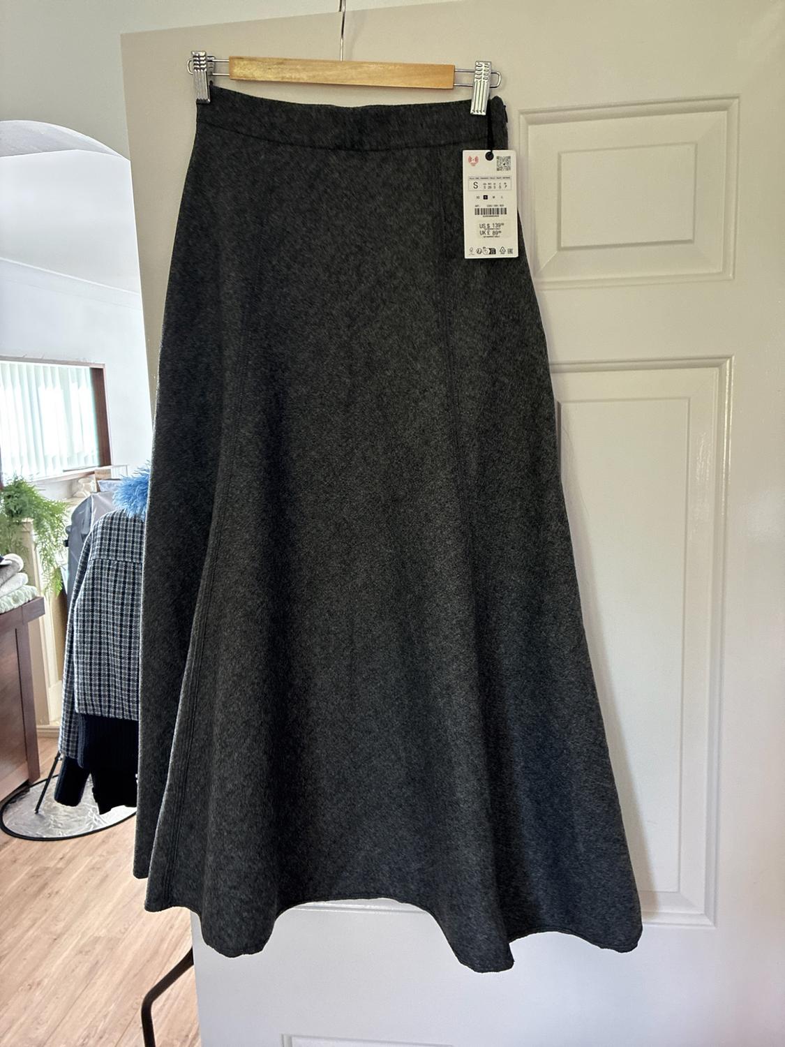 Dark grey flared maxi skirt hanging on a white door. Label with text "S",
"US $ 139", "UK £ 89".