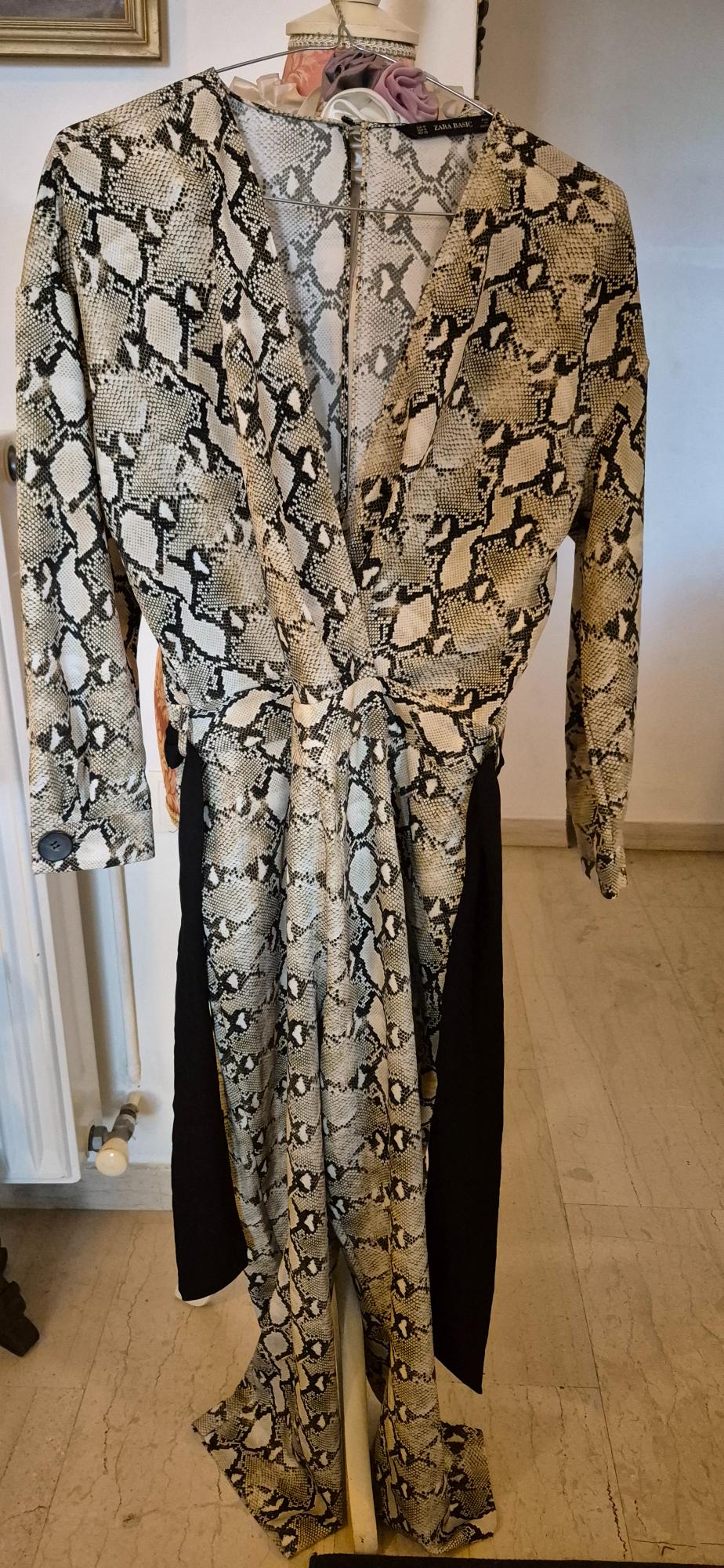 Jumpsuit with snake print in beige and black tones, hanging on a hanger. Interior background of a room.