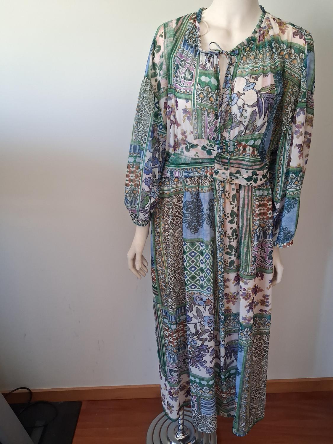 Mannequin with a long floral and geometric print dress in green, blue, and purple tones, with a white background.