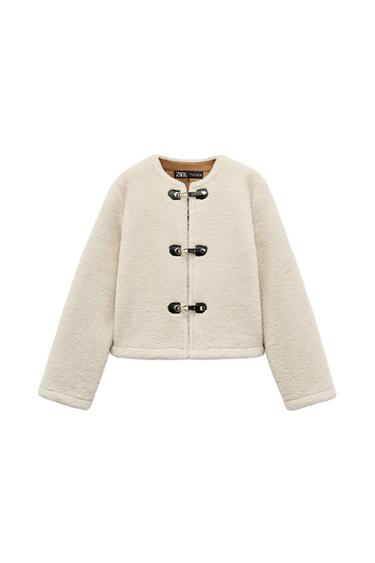 Front view of a beige jacket with black buckle fastenings.