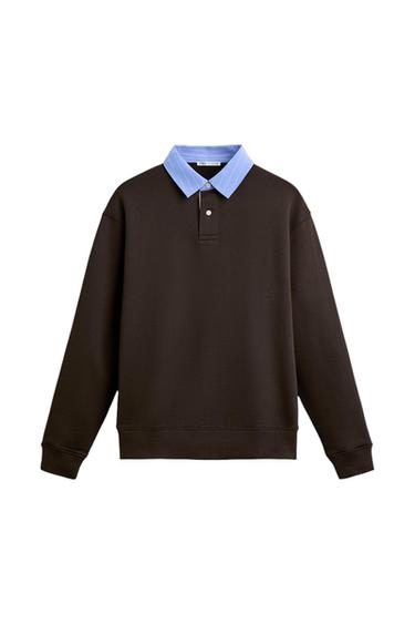 Black sweatshirt with a light blue shirt collar and buttons. Visible label on the collar. White background.