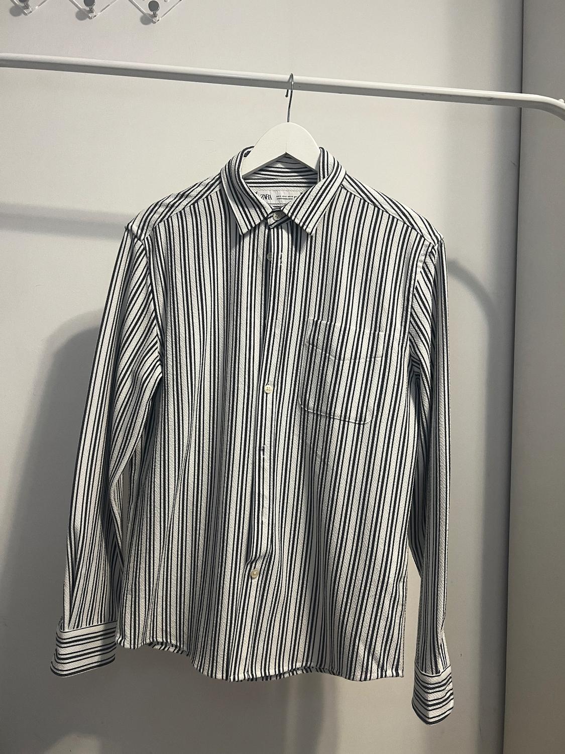 Black and white striped shirt hanging on a white hanger against a light grey background.