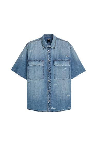 Light blue denim shirt with short sleeves, two large front pockets, and buttons. Visible inner label with the text "ZARA".