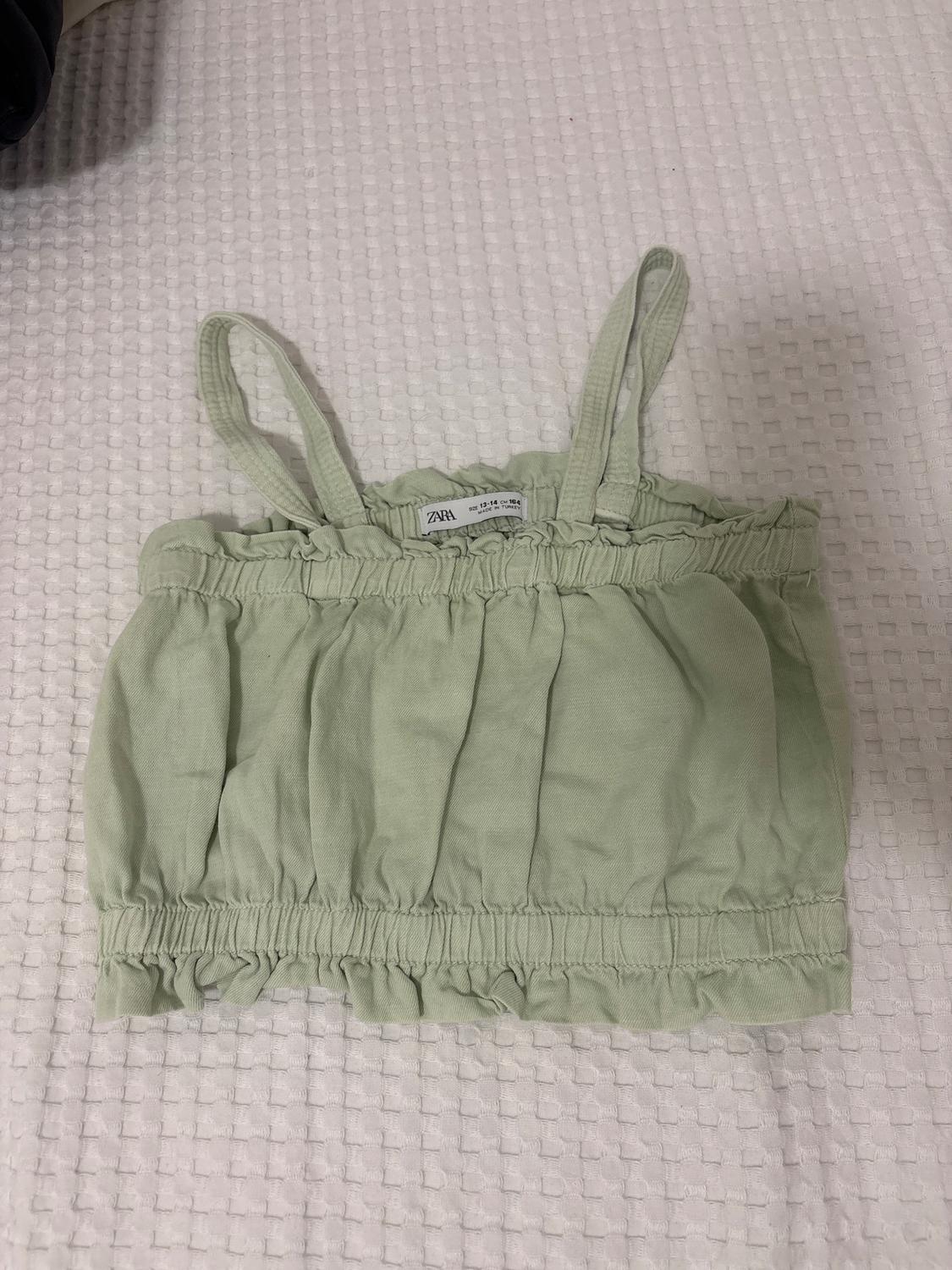 Light green crop top with spaghetti straps on a textured white surface. Visible label with the ZARA brand.