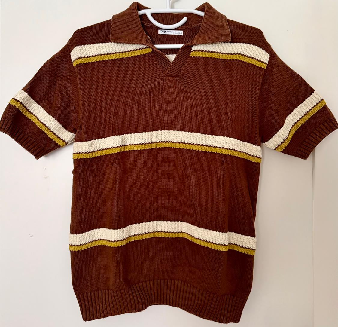 Brown polo shirt with horizontal cream and mustard stripes, hanging on a white hanger against a white background.