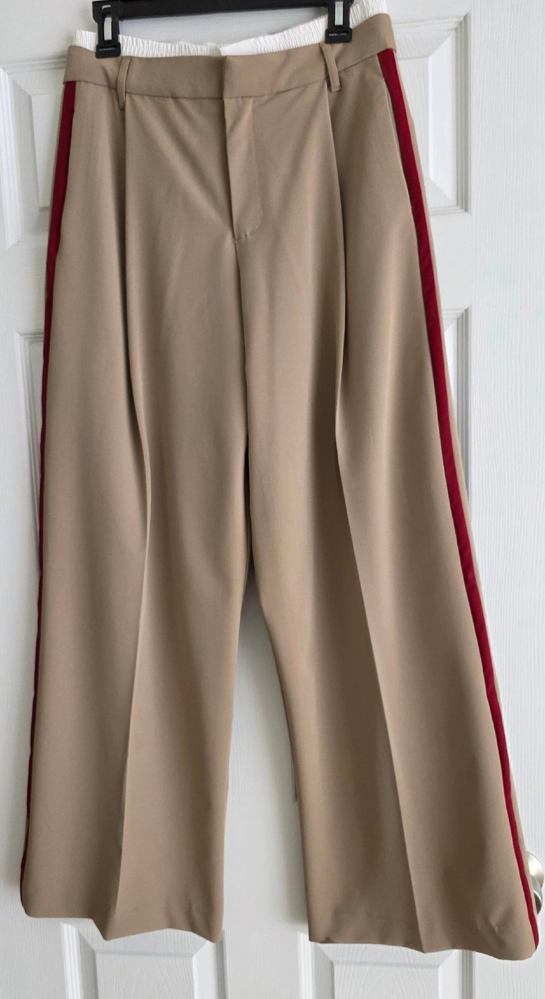 Beige pants with red stripes on the sides, hanging on a hanger over a white door.