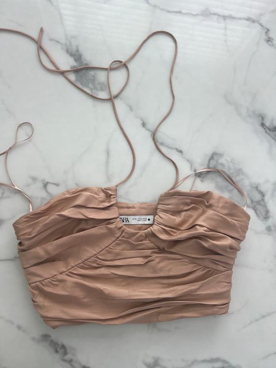 Beige spaghetti strap top with pleats, on a white and gray marble background. Visible label inside.