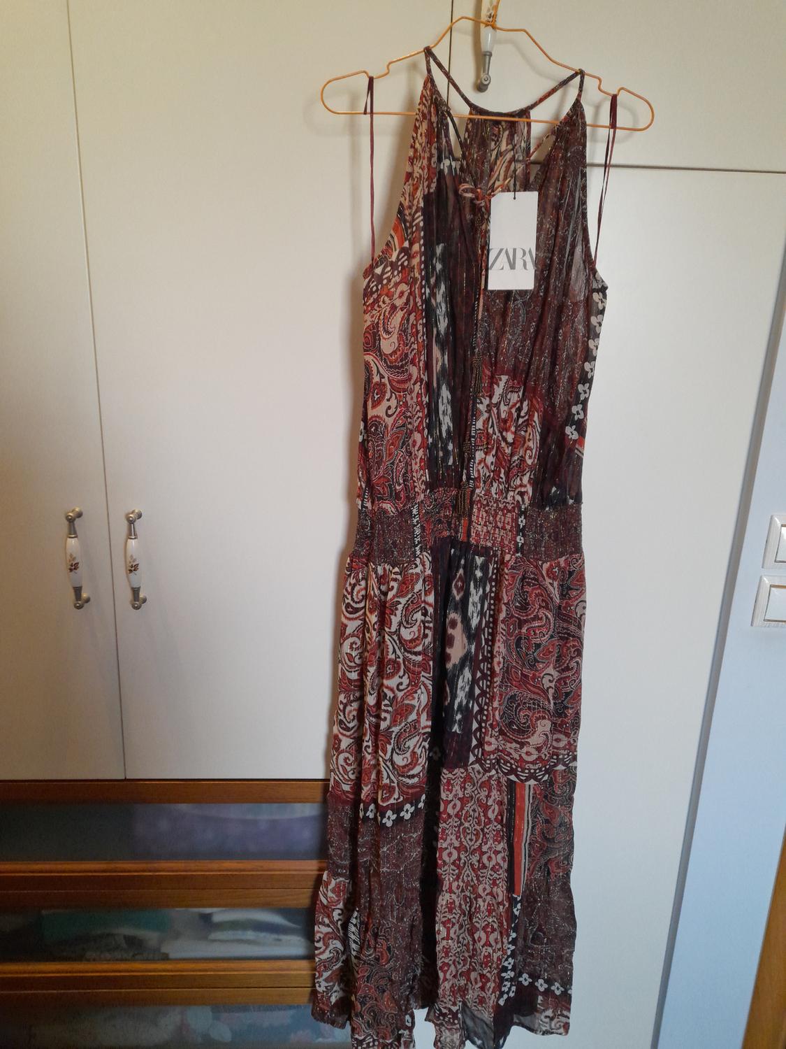 Long dress with a red and brown paisley print, hanging on a gold hanger. Visible label with text "ZVR".
