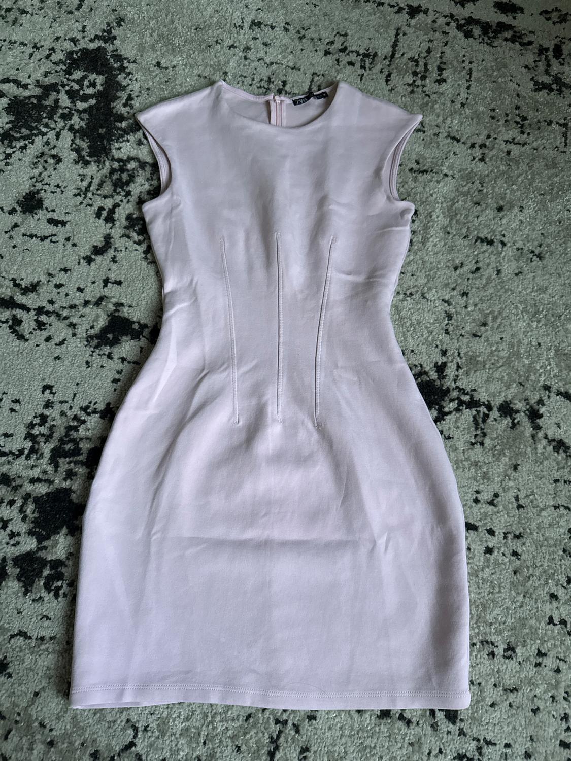 Light lilac sleeveless dress on a textured grey and black rug. Visible zip at the upper back.