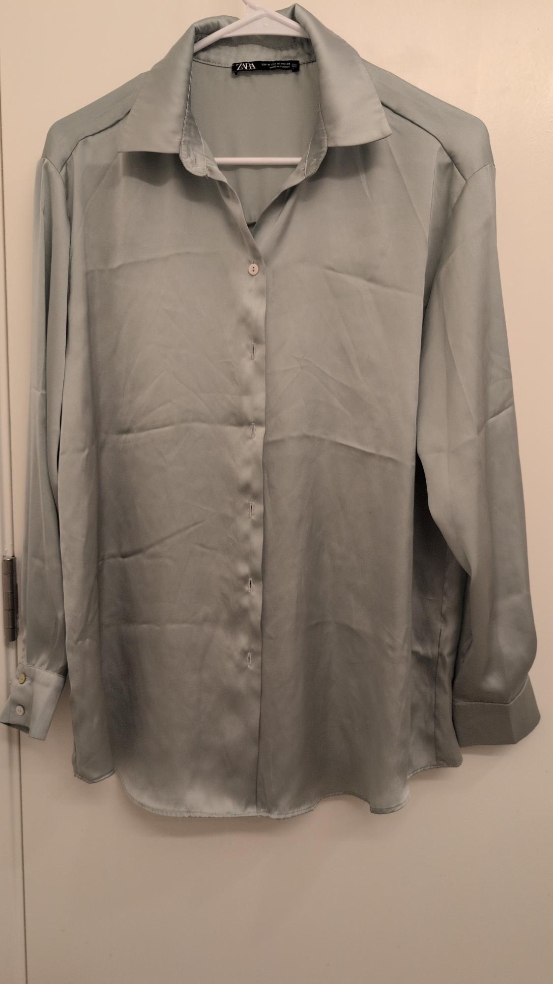 Long-sleeved gray shirt hanging on a white hanger, with front buttons and a classic collar. Label visible on the inside of the neck.
