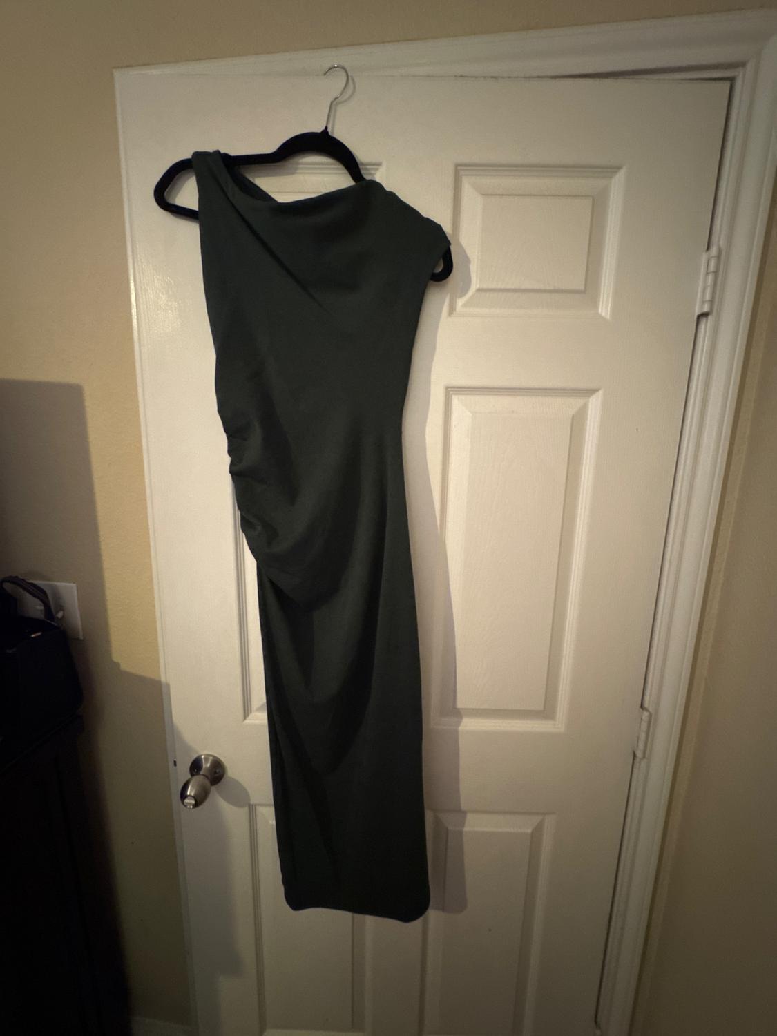 Sleeveless black dress hanging on a hanger over a white door. The light creates soft shadows on the wall.