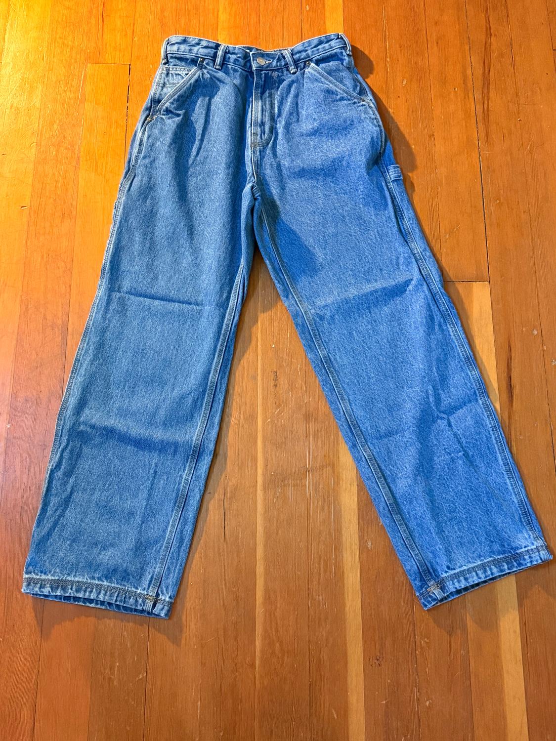 Blue straight-cut jeans on a light wooden floor.