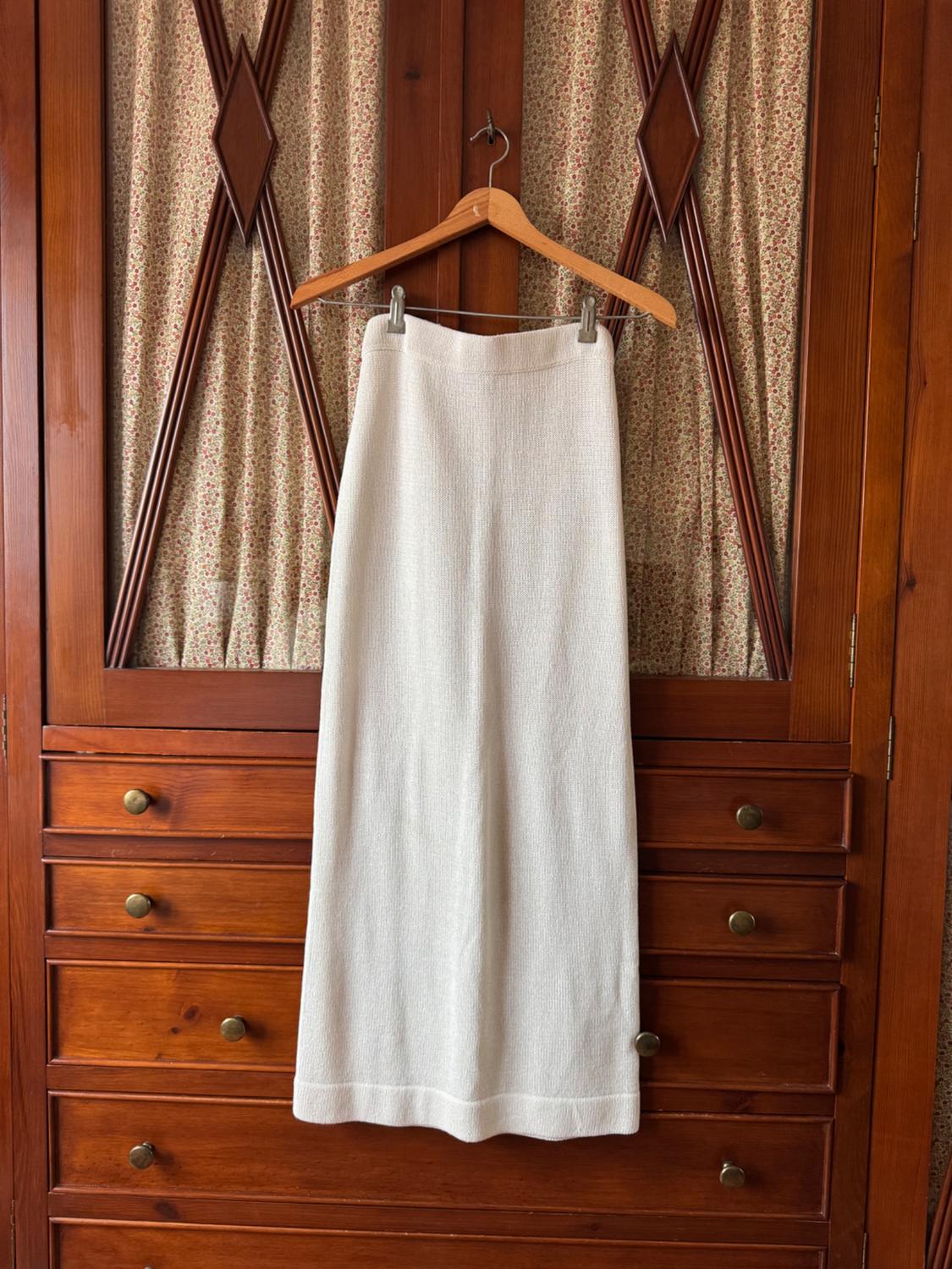 A long white skirt hanging on a wooden hanger in front of a wooden wardrobe with floral print fabric details.
