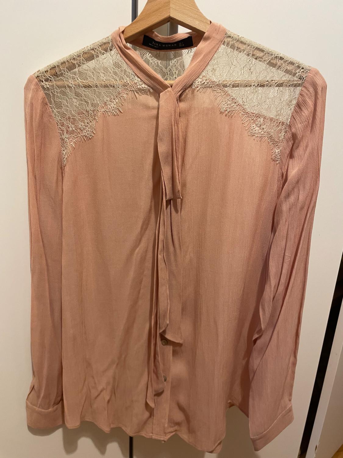 Front view of a pink blouse with lace on the shoulders and a bow at the neck.