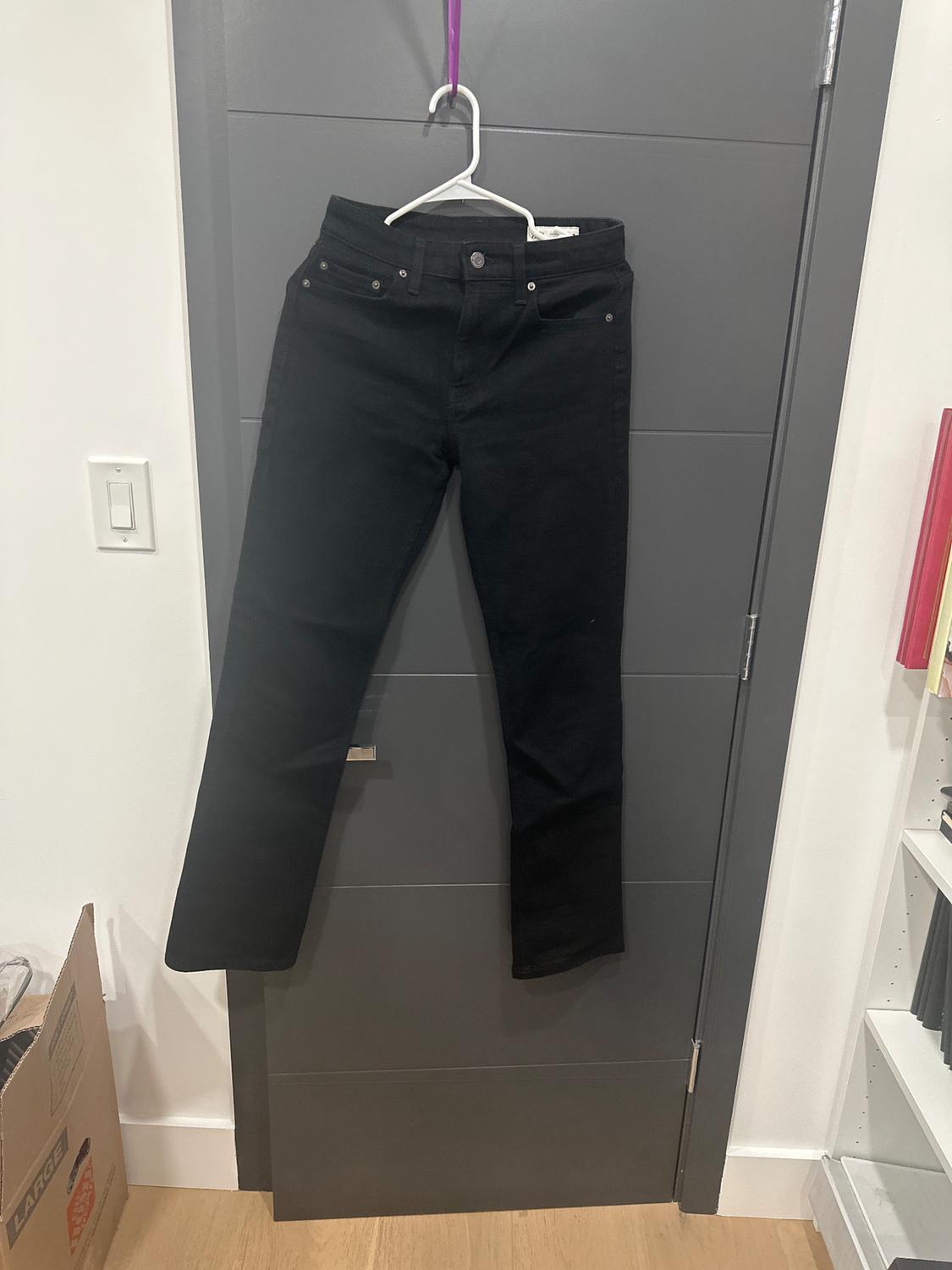 Black pants hanging on a white hanger over a gray door. Cardboard box and white shelving visible on the sides.