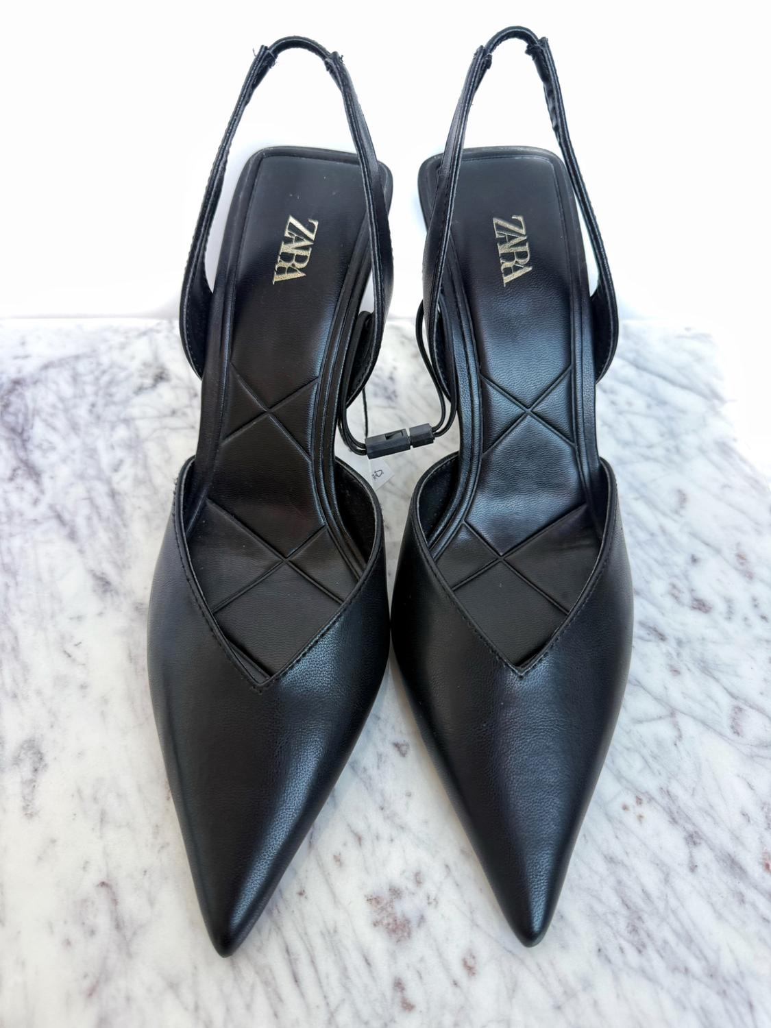 Black heeled shoes with pointed toes and back straps, on a marble background. The insole has the "ZARA" logo.