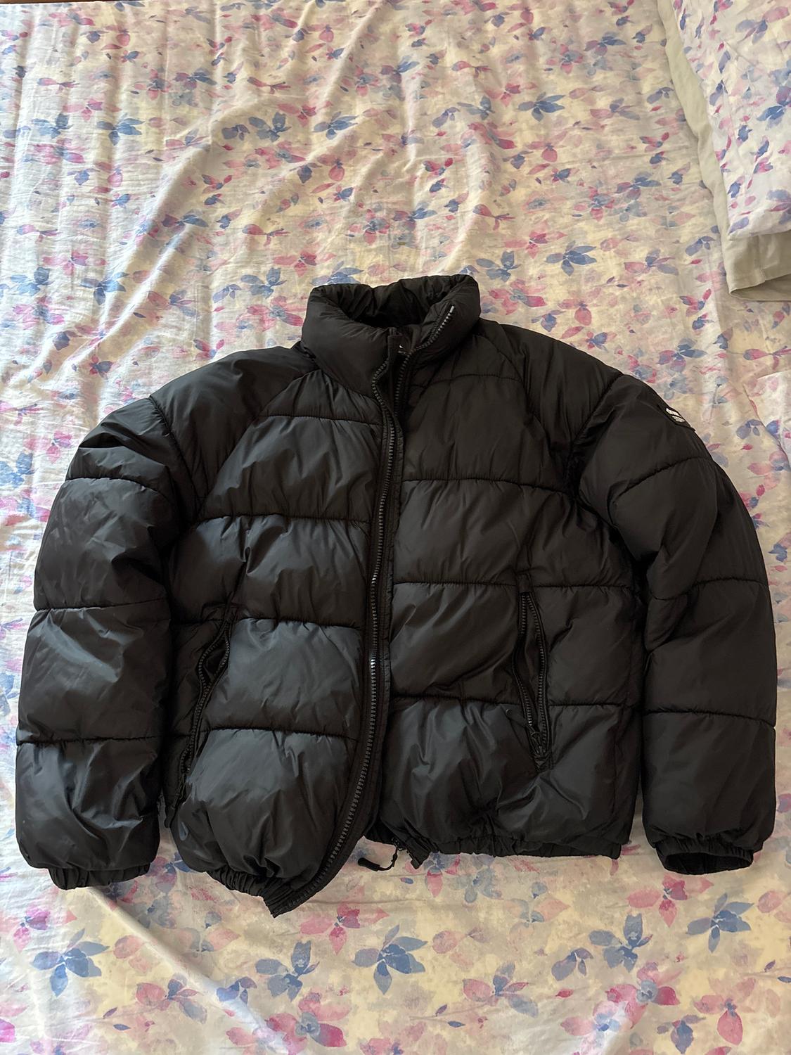 Black padded jacket with a zip, on a floral print quilt in shades of pink and blue.