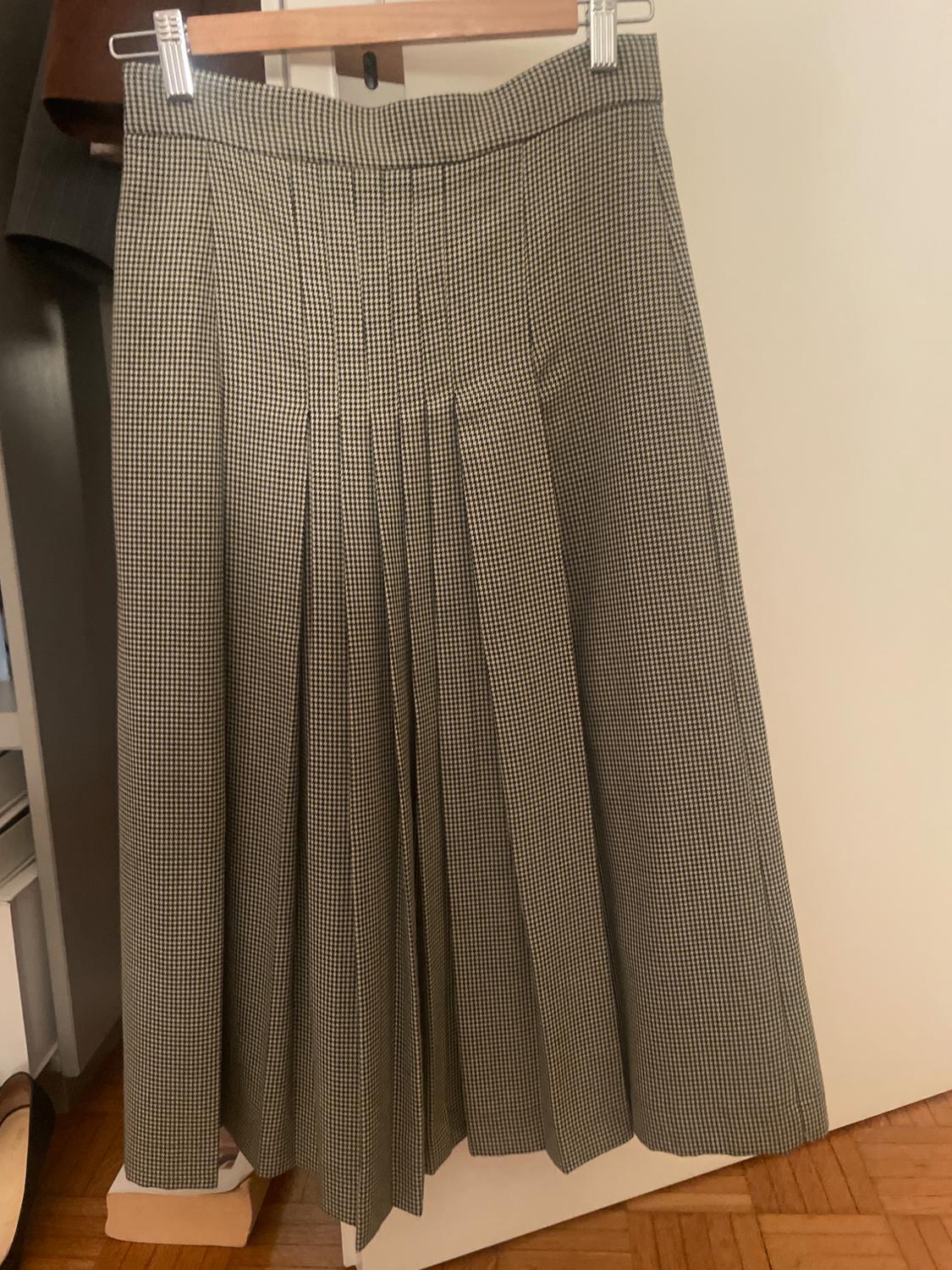 Black and white small checked pleated skirt hanging on a wooden hanger, against a wardrobe and wooden floor background.