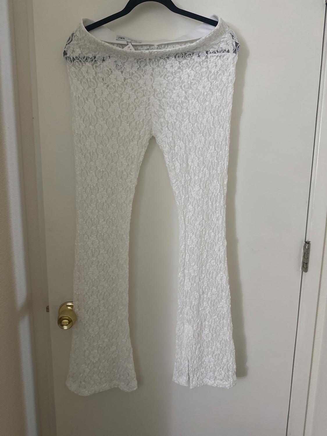 White lace flared trousers hanging on a black hanger over a white door with a gold doorknob.