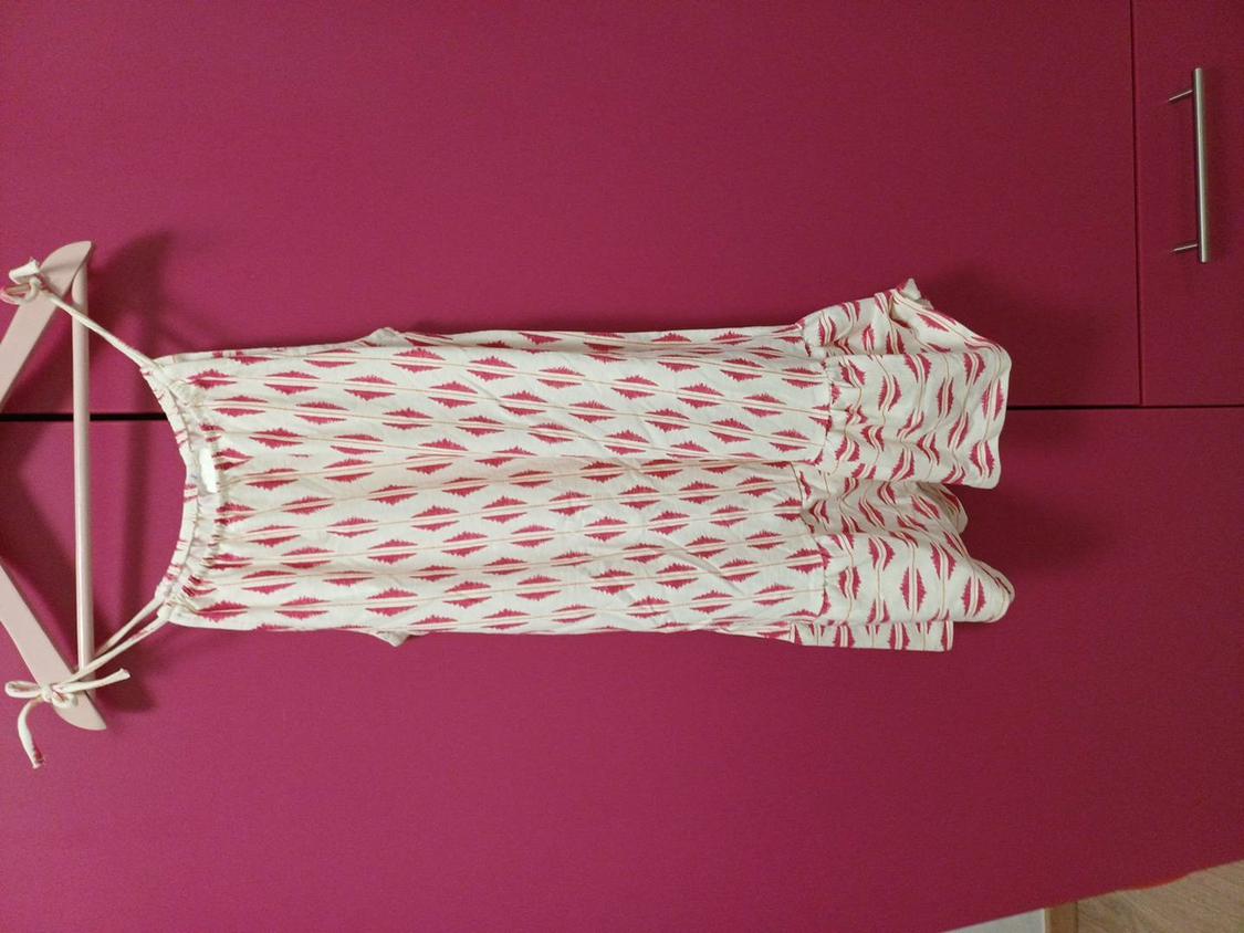 Red and white geometric print sleeveless dress, hanging on a hanger in front of a pink wardrobe.