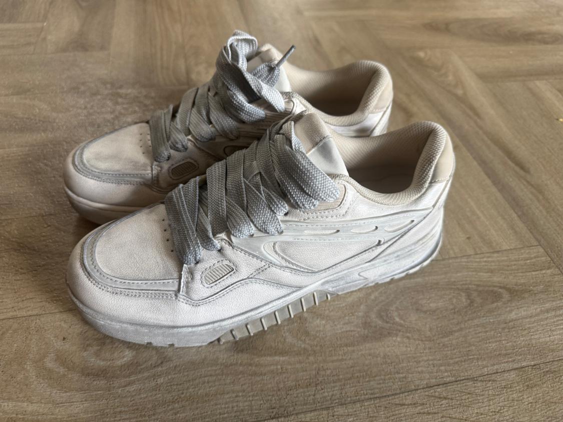 White sports trainers with grey laces on a light wooden floor. Modern and casual design.