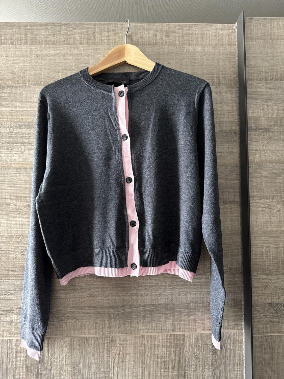 Dark grey cardigan with light pink trim and front buttons, hanging on a wooden hanger against a wooden background.