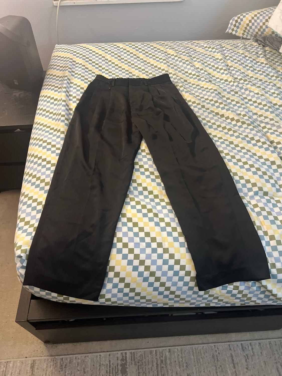 Black pants laid out on a bed with blue, green, and white plaid sheets.
