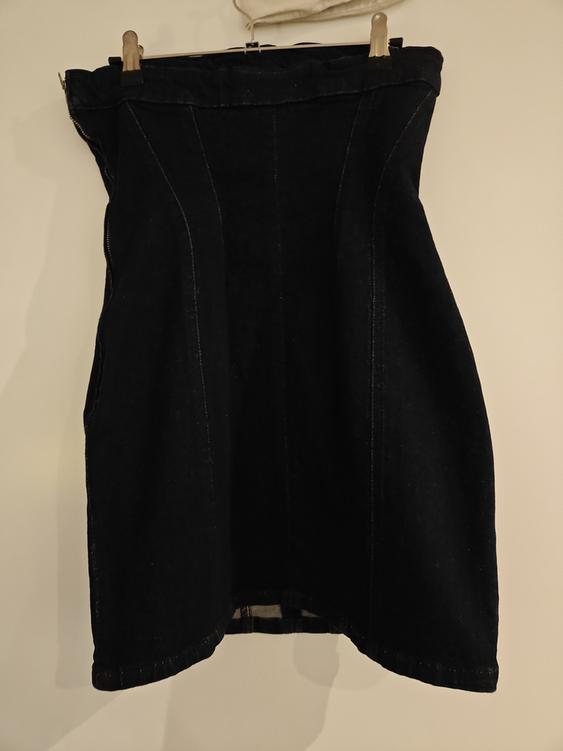 Black denim skirt hanging on a hanger against a white background. The skirt has visible seams and a flared design.