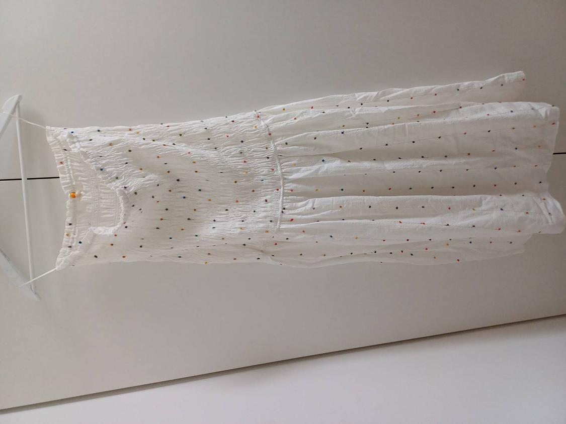 White dress with straps, featuring a small colourful polka dot print, hanging on a white hanger against a neutral background.