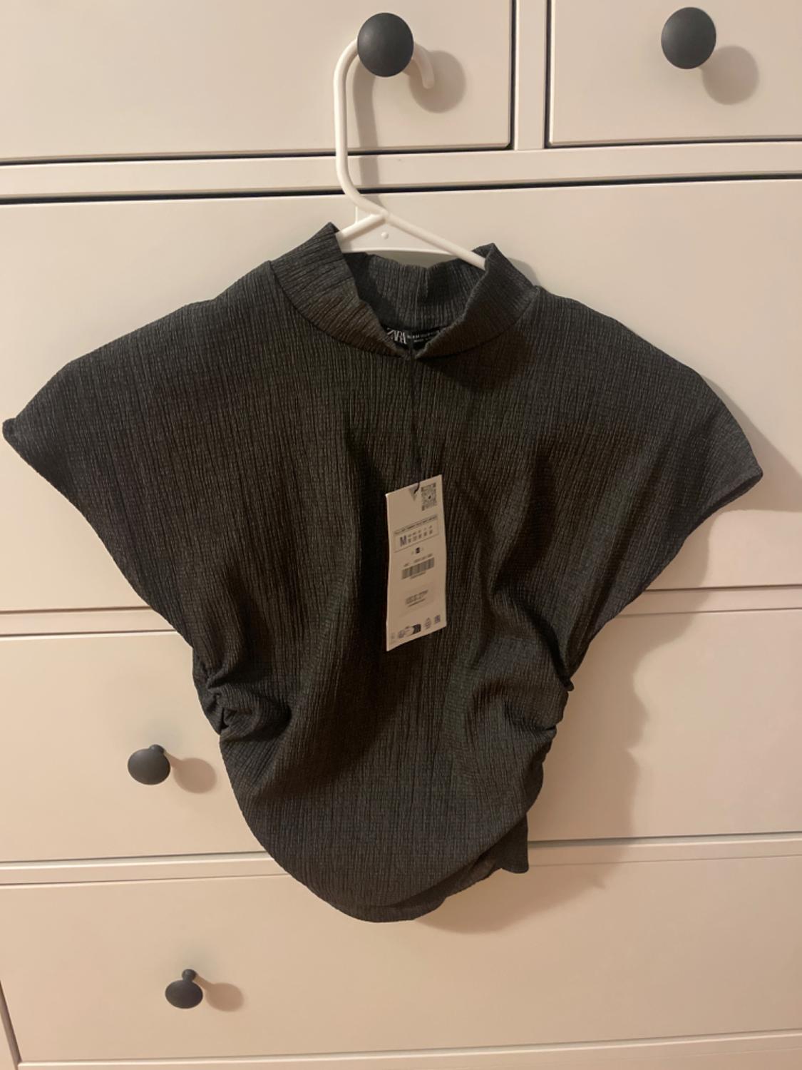 Front view of a dark, high-necked, short-sleeved blouse on a hanger.