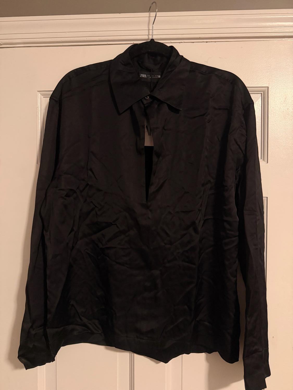 A crumpled black long-sleeved shirt with a V-neck, hanging on a hanger on a white door. Visible label with the text ZARA.