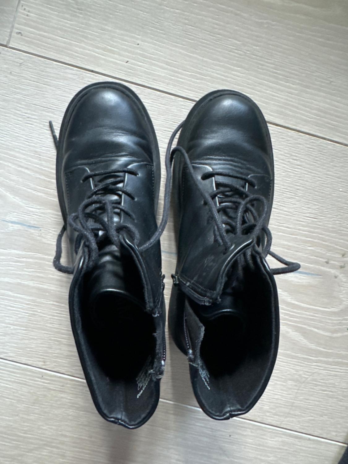 Black leather lace-up boots seen from above on a light wooden floor.