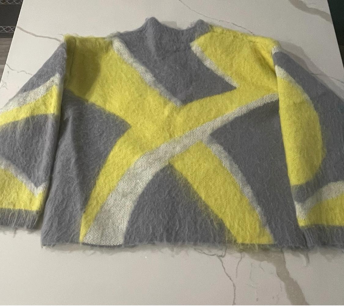 Woollen jumper with an abstract design in grey and yellow on a white surface. Long sleeves and a high neck.