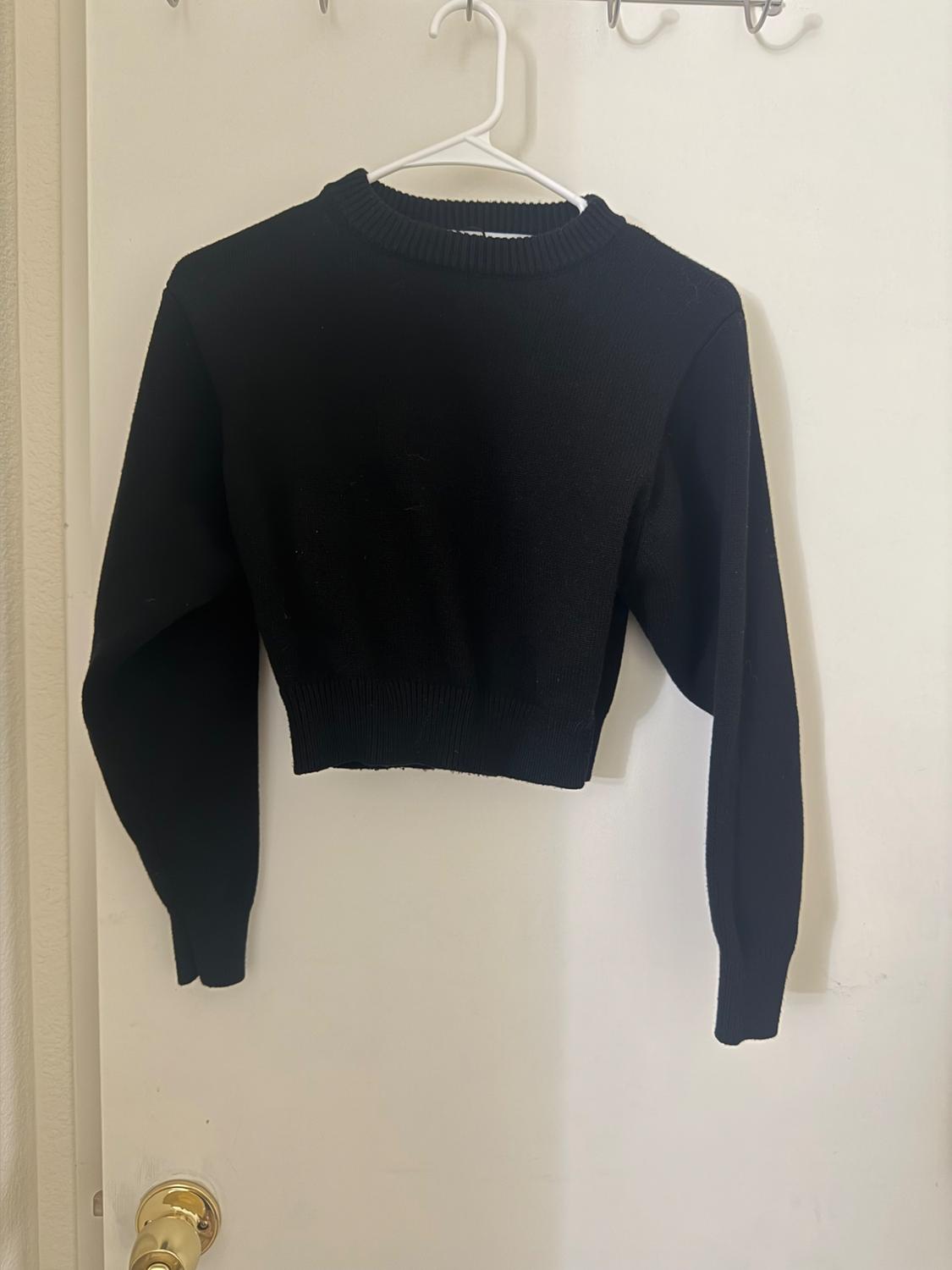Black, long-sleeved jumper hanging on a white coat hanger over a white door with a gold door knob.