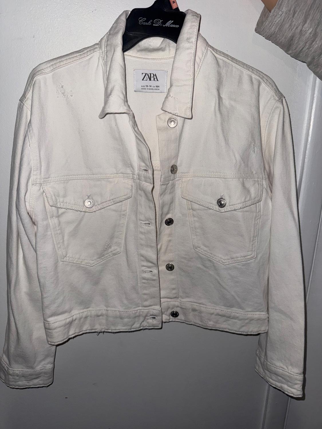 Arm holding a white denim jacket on a hanger. Text: Carlo De Marco, ZARA, SIZE 13-14 CM 164, MADE IN BANGLADESH.