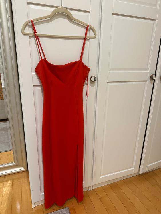 Long red dress with thin straps and a side slit, hanging on a hanger in front of a white paneled-door wardrobe.