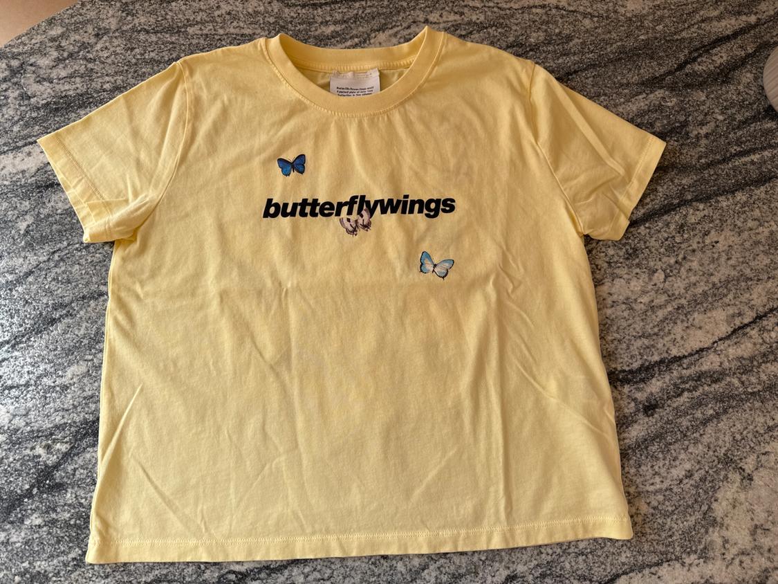 Yellow T-shirt on a grey marble background, with "butterflywings" text and two blue butterflies printed on the front.
