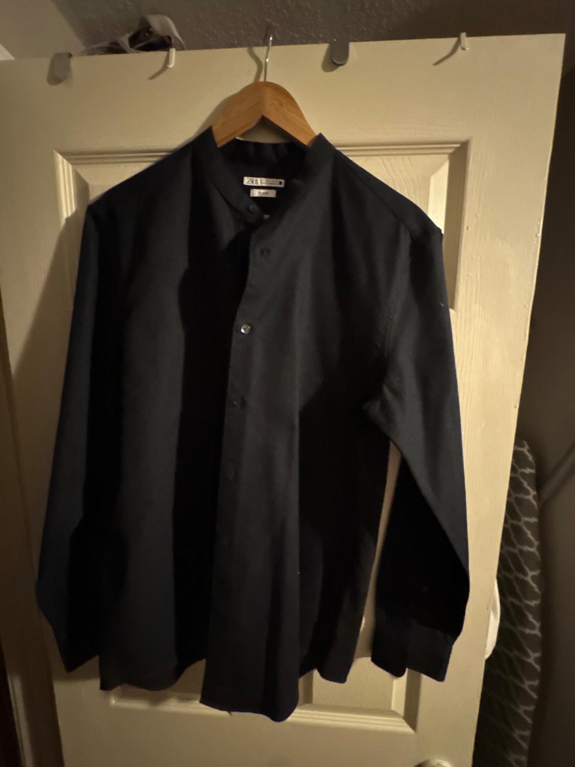 Black long-sleeved shirt hanging on a wooden hanger over a white door. Dim, warm atmosphere.